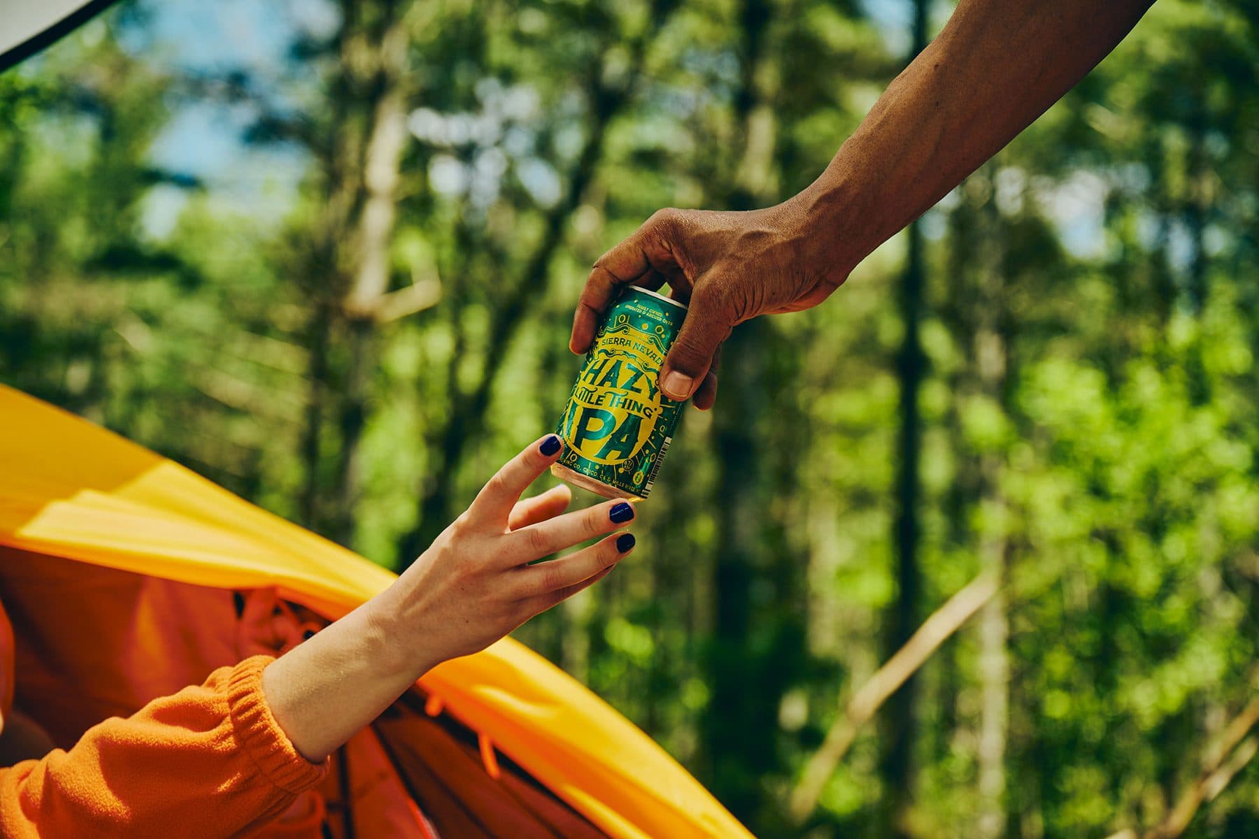 Handing off a can of Sierra Nevada Hazy Little Thing IPA to a person in a camping tent